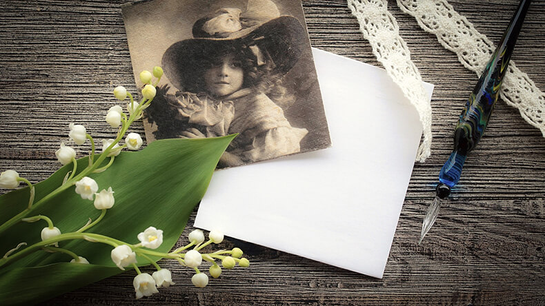 Vintagetyylinen kuva, kuvassa kieloja, mustavalkoinen kortti, pitsiä, kynä ja valkoinen pieni paperiarkki.
