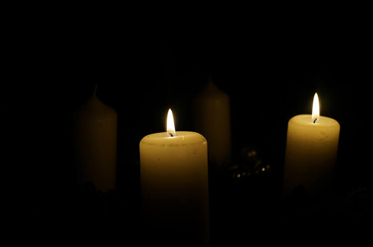 Kaksi valkoista kynttilää ja niiden heijastukset tummalla taustalla.