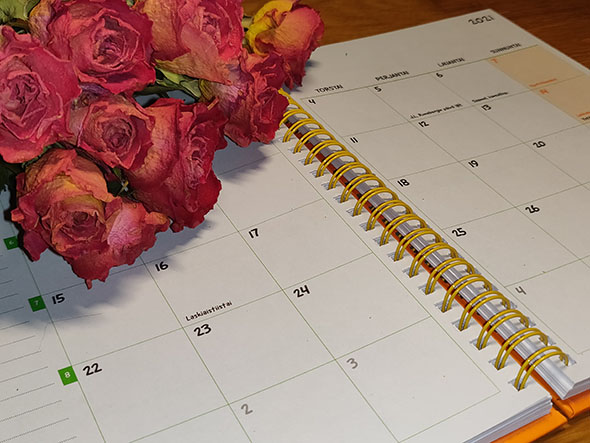 Avoin kalenteri ja kimppu punertavia kuivattuja ruusuja.