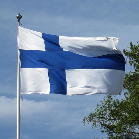 Suomen lippu tuulessa kesäisessä maisemassa.