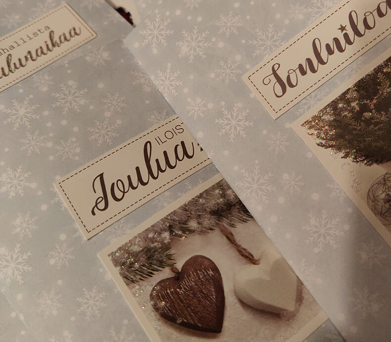 Sinivalkoisia itsetehtyjä joulukortteja, joissa tekstit Iloista joulua ja Jouluiloa. Korteissa myös kuva ruskeasta ja valkoisesta sydämestä.