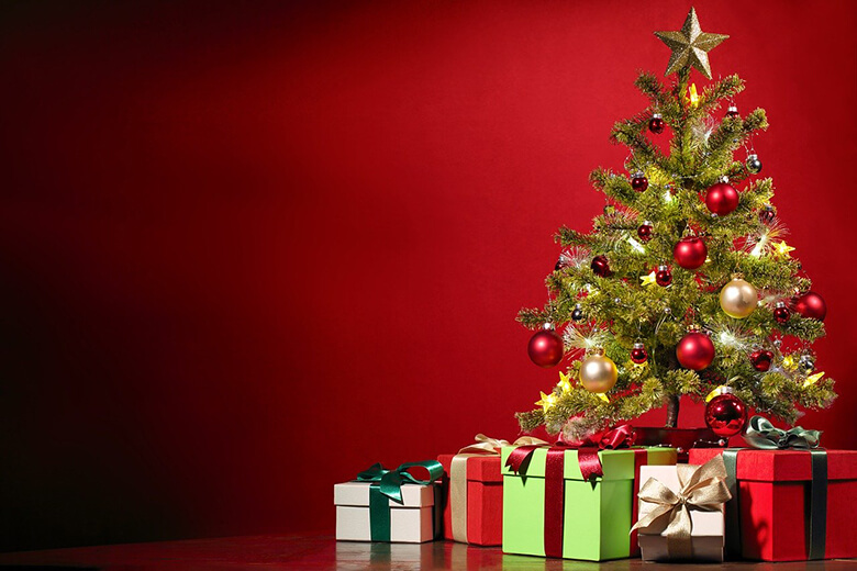 Punaisin, kultaisin ja valkoisin koristeltu joulukuusi punaisella taustalla, joulukuusen ympärillä useita lahjapaketteja.