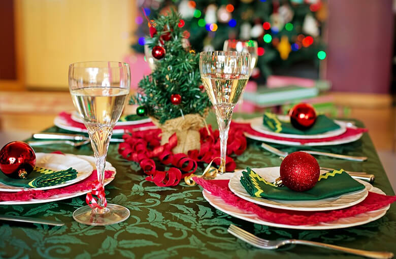Vihrein, valkoisin ja punaisin astioin ja liinoin koristeltu joulupöytä, keskellä kaksi juomalasia täynnä kouhuvaa juotavaa.