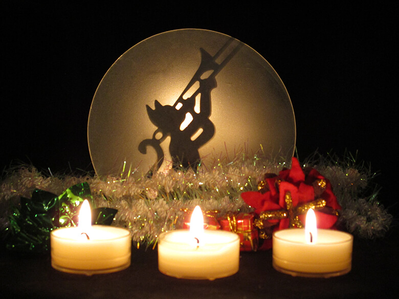 Kolme palavaa tuikkukynttilää, taustalla joulukoristeita ja torvea soittava kissakoriste.