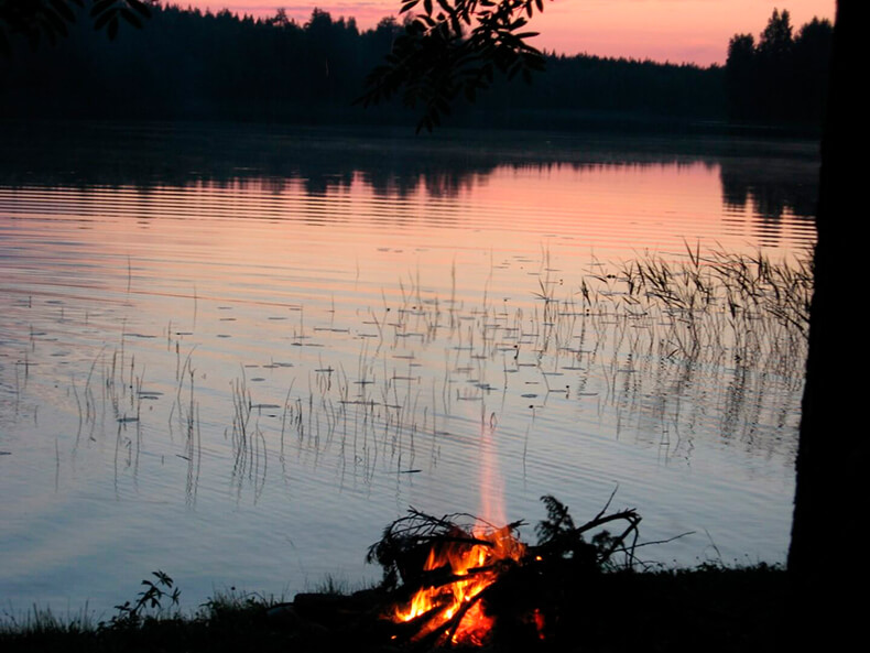 Pieni juhannuskokko järven rannalla auringonlaskun aikaan.