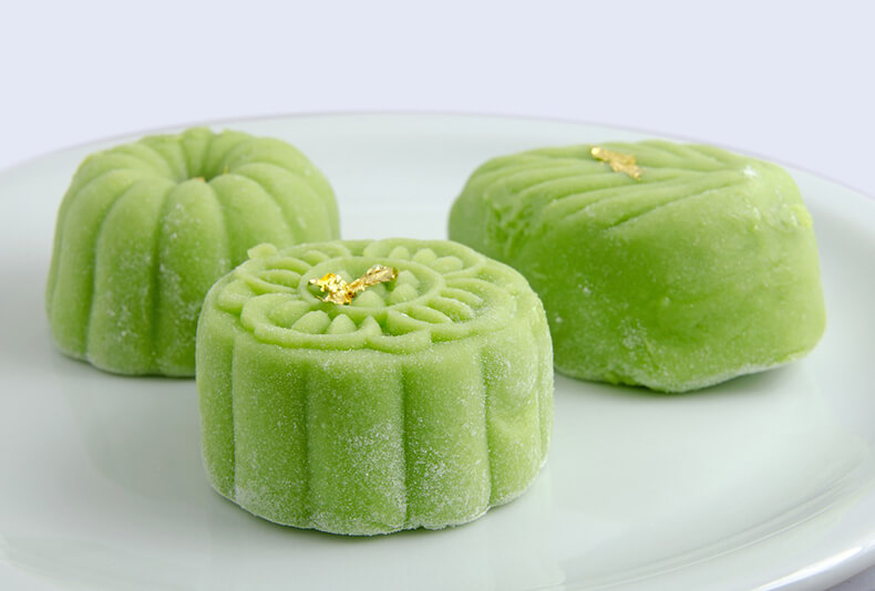 Kolme pientä kiinalaista perinteistä leivosta eli kuukakkuja värjättynä vihreiksi ja kauniisti koristeltuina.