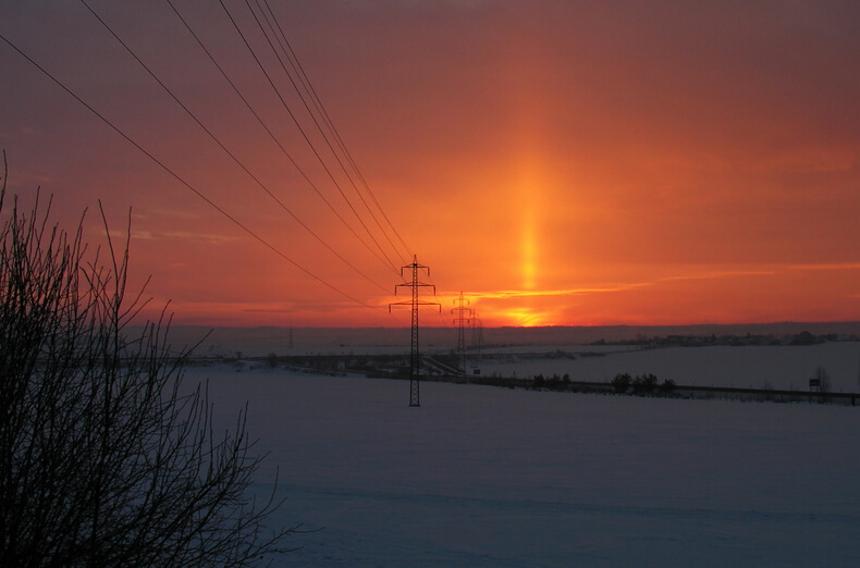 Talvinen maisema auringonlaskun aikaan, taustalla punaoranssi taivas ja auringonpilari.