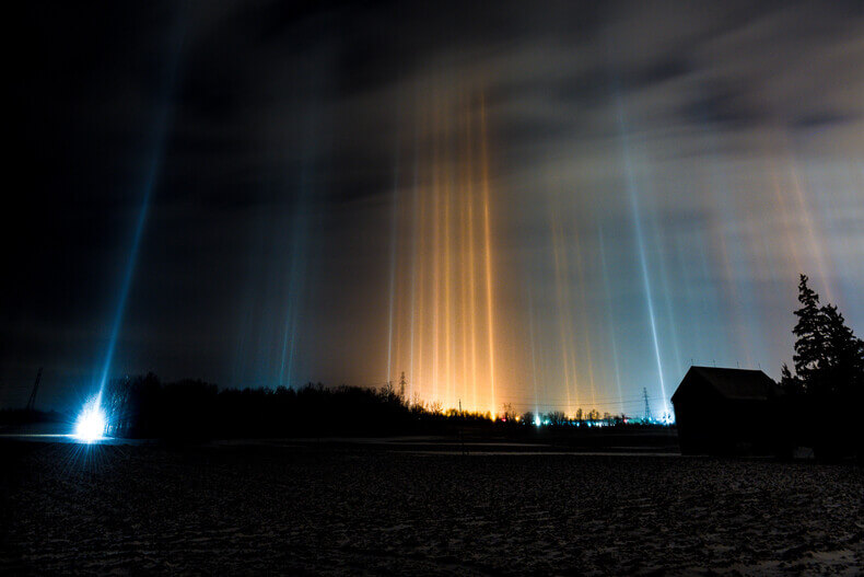 Tumma yömaisema, jossa ylös kohti taivasta nousee useita värikkäitä valopilareita.
