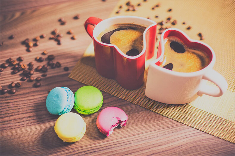 Kaksi sydämenmuotoista kahvikuppia ja macaron-keksejä.