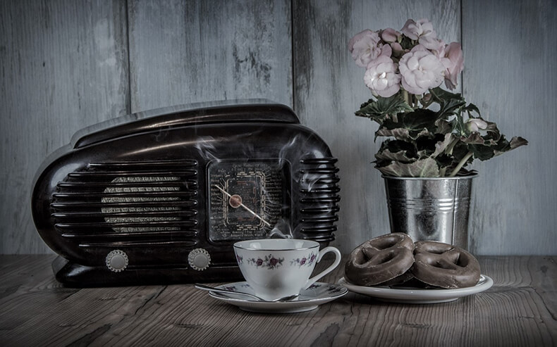 Vanhan ajan radio, kahvikuppi, rinkeleitä ja kukkakimppu.