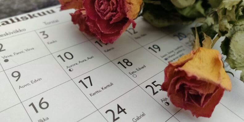 Nimipäiväkalenteri ja kuivattuja punaoransseja ruusuja.