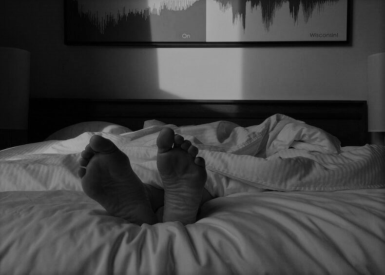 Ihminen nukkumassa peiton alla, vain jalat näkyvät.