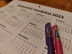 Kalenteri vuodelle 2023 ja kaksi värikästä kynää.